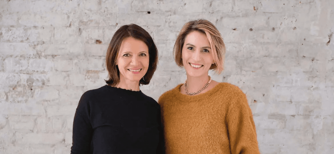 Frida Lüth und Ulrike Vollmoeller, Gründerinnen von IRIS&FRED, Portrait zweier Frauen vor einer hellen Backsteinwand.