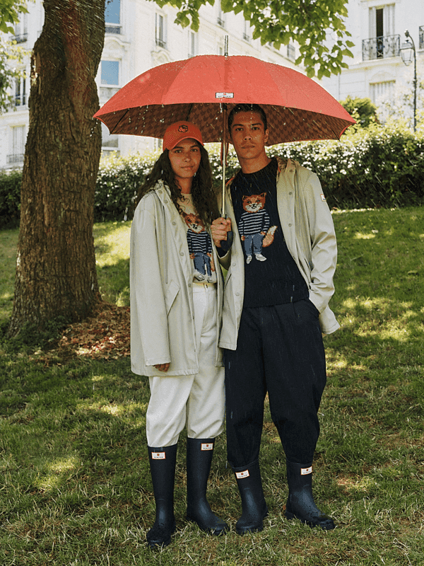 Un homme et une femme équipés de cirés, bottes de pluie et parapluie posent dans un parc