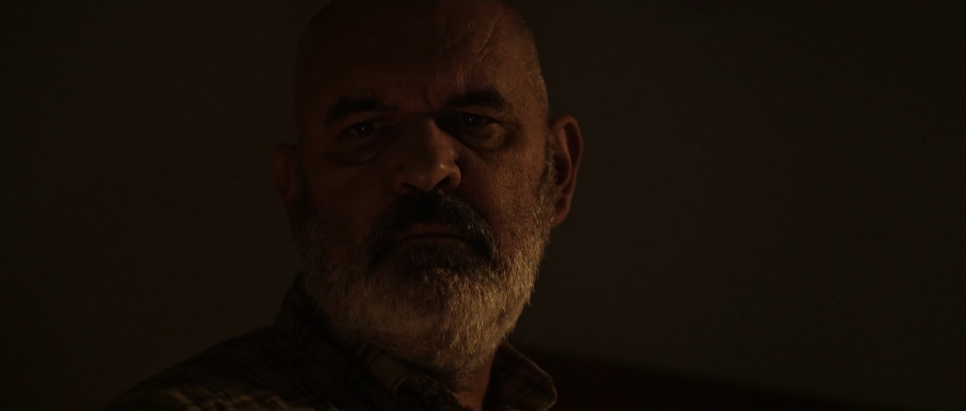 Portrait of an older man sitting in a dimly lit room, dramatic cinematography.