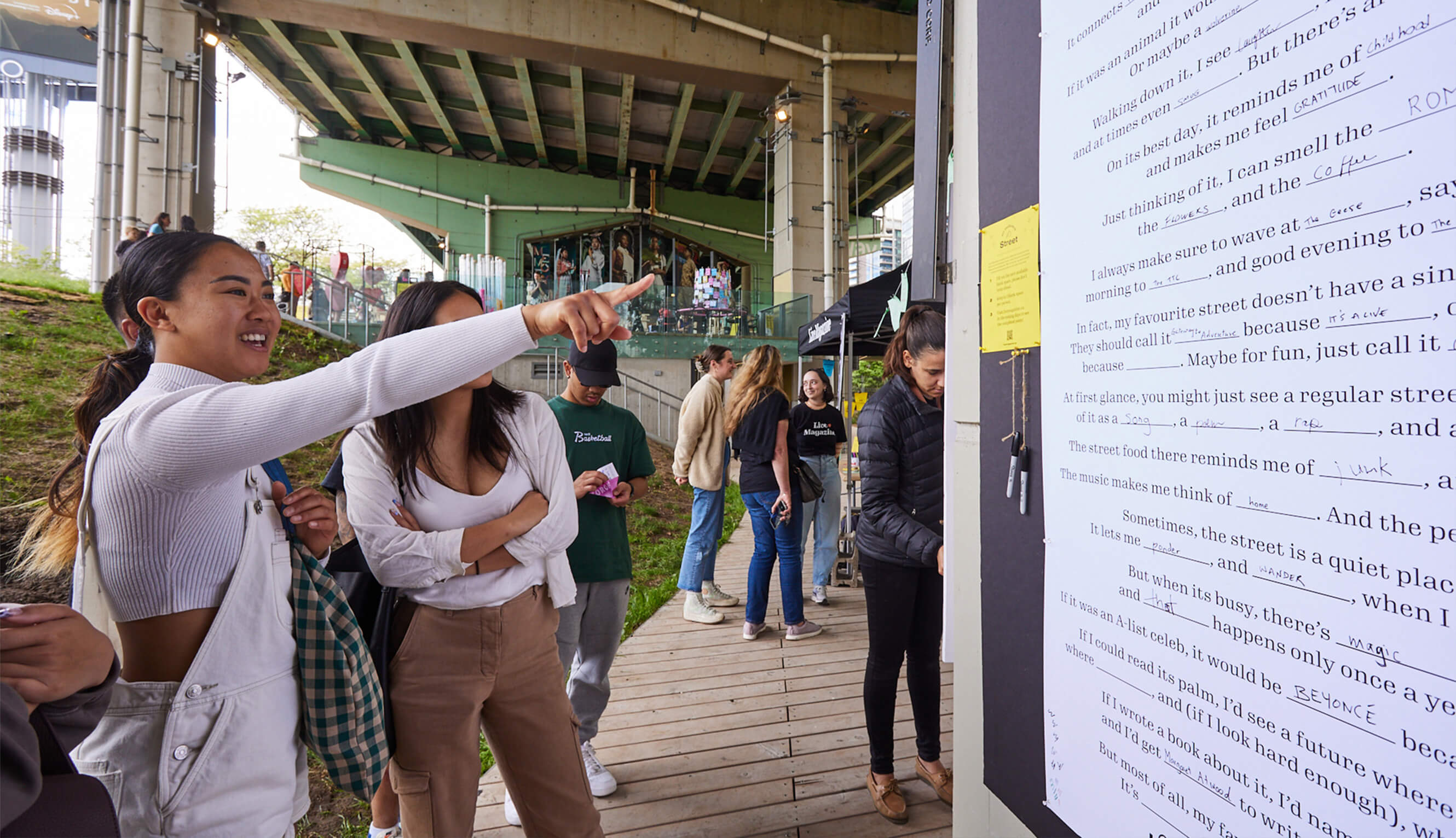 Two people standing in front of a Live Magazine activation, pointing up at people's answers.