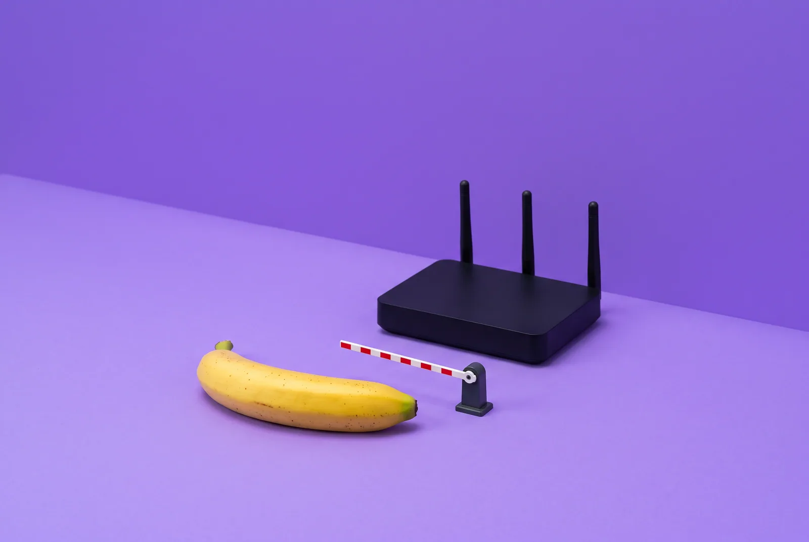 A banana stopped by a lowered striped barrier next to a black Wi-Fi router, how to block porn on your router