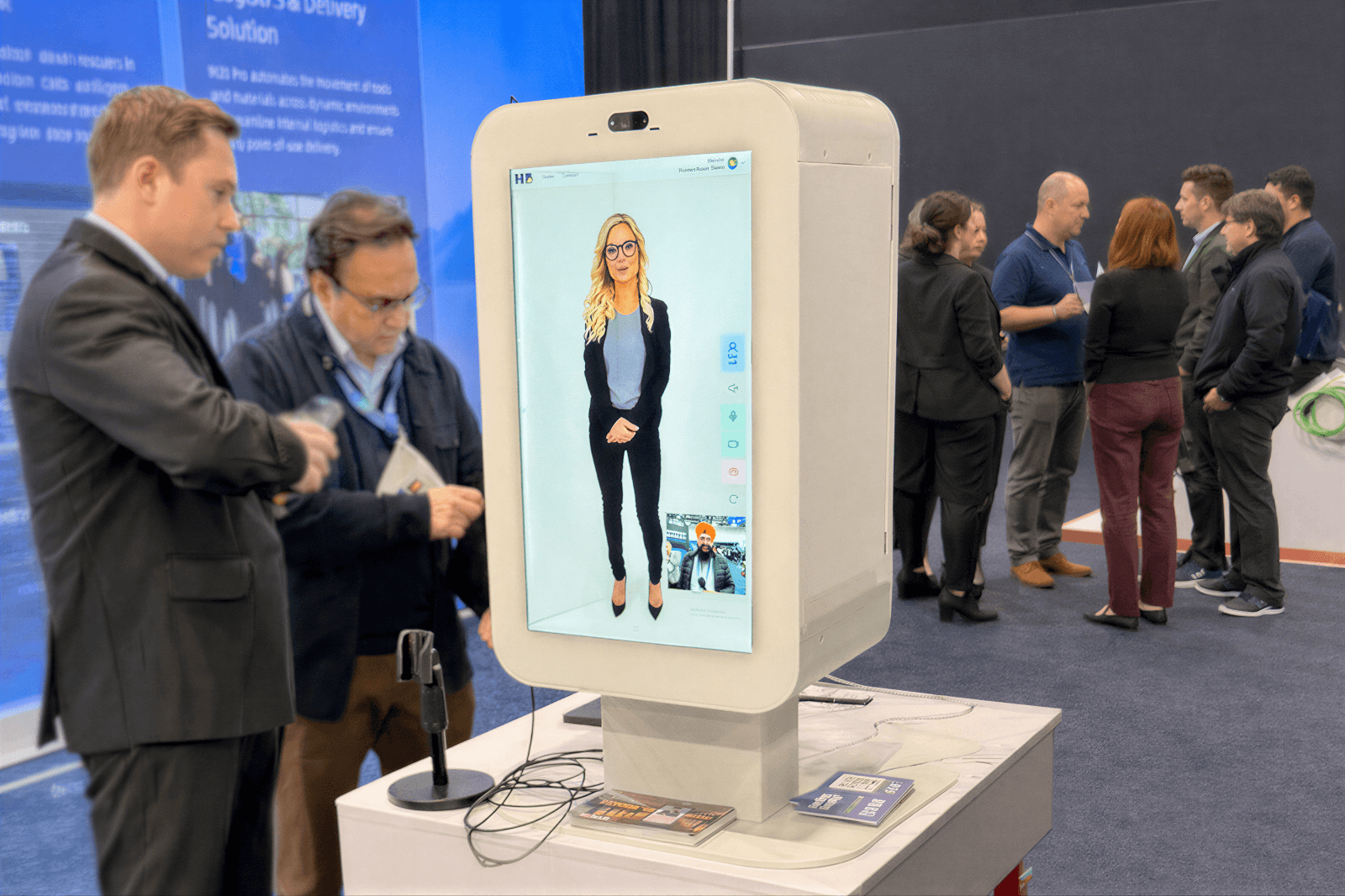 AI-powered HumanBeam holographic host displayed on a digital kiosk interacting with attendees at a technology event, demonstrating conversational event engagement and automated speaker or sponsor introductions.