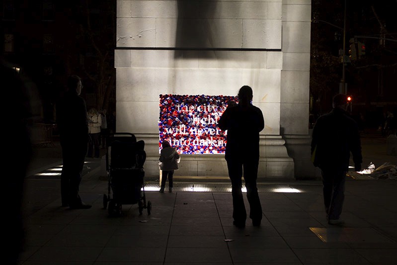 An illuminated and colorful street poster with text on it near a building. Also some people look at it.