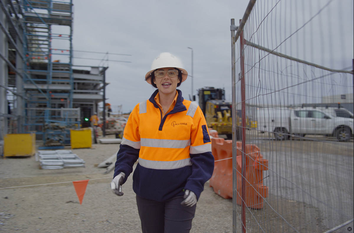 ACCIONA construction worker in hi-vis PPE walking on site behind fencing