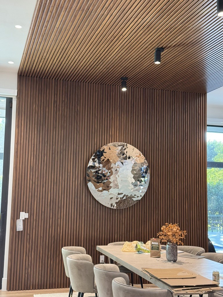 Circular faceted metallic sculpture mounted on a wood-slat accent wall in a dining area