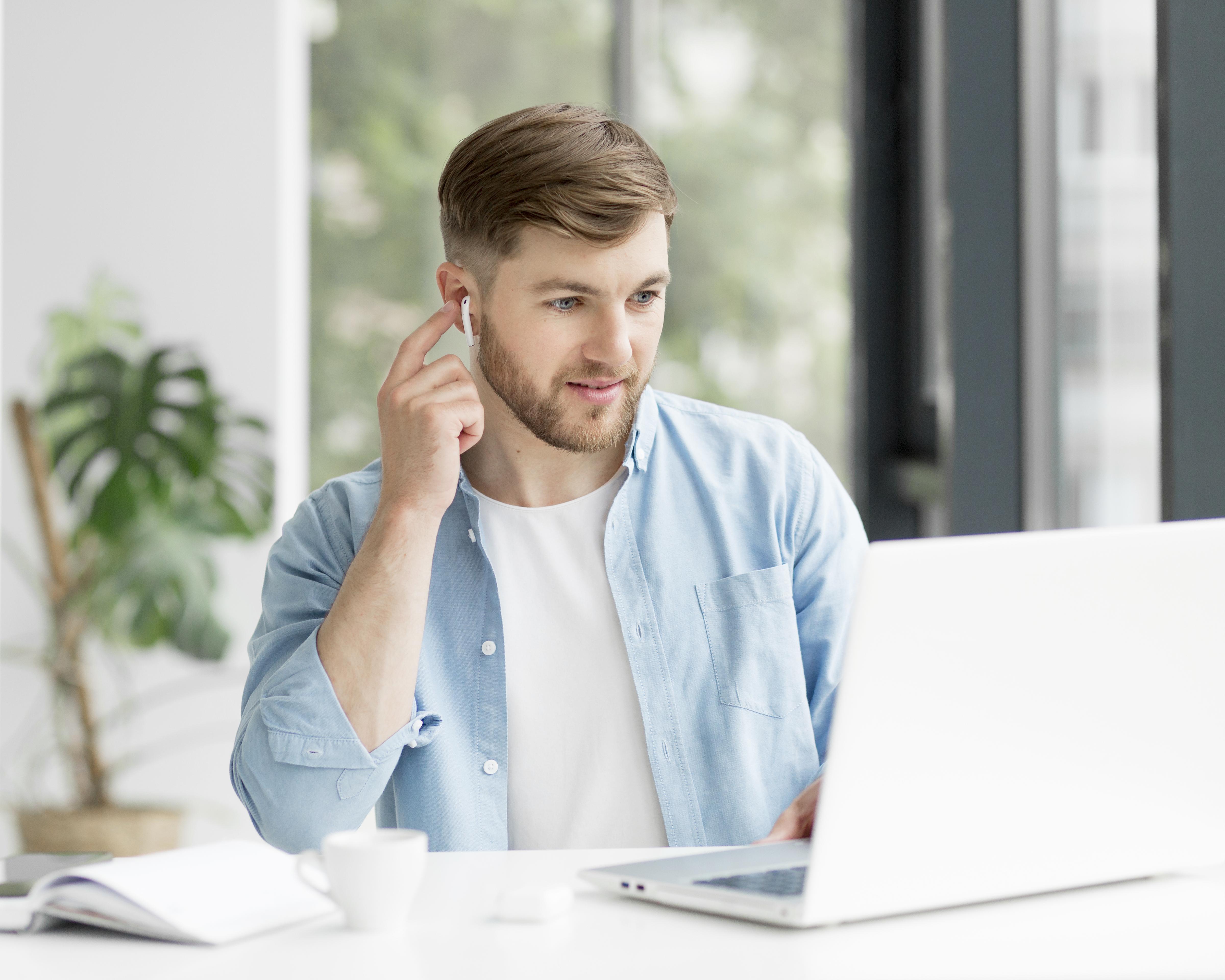 Man using earbuds while working on a laptop.