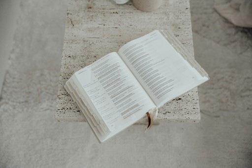 Eine aufgeschlagene Bibel mit Registertaben liegt auf einem hellen Steintisch.