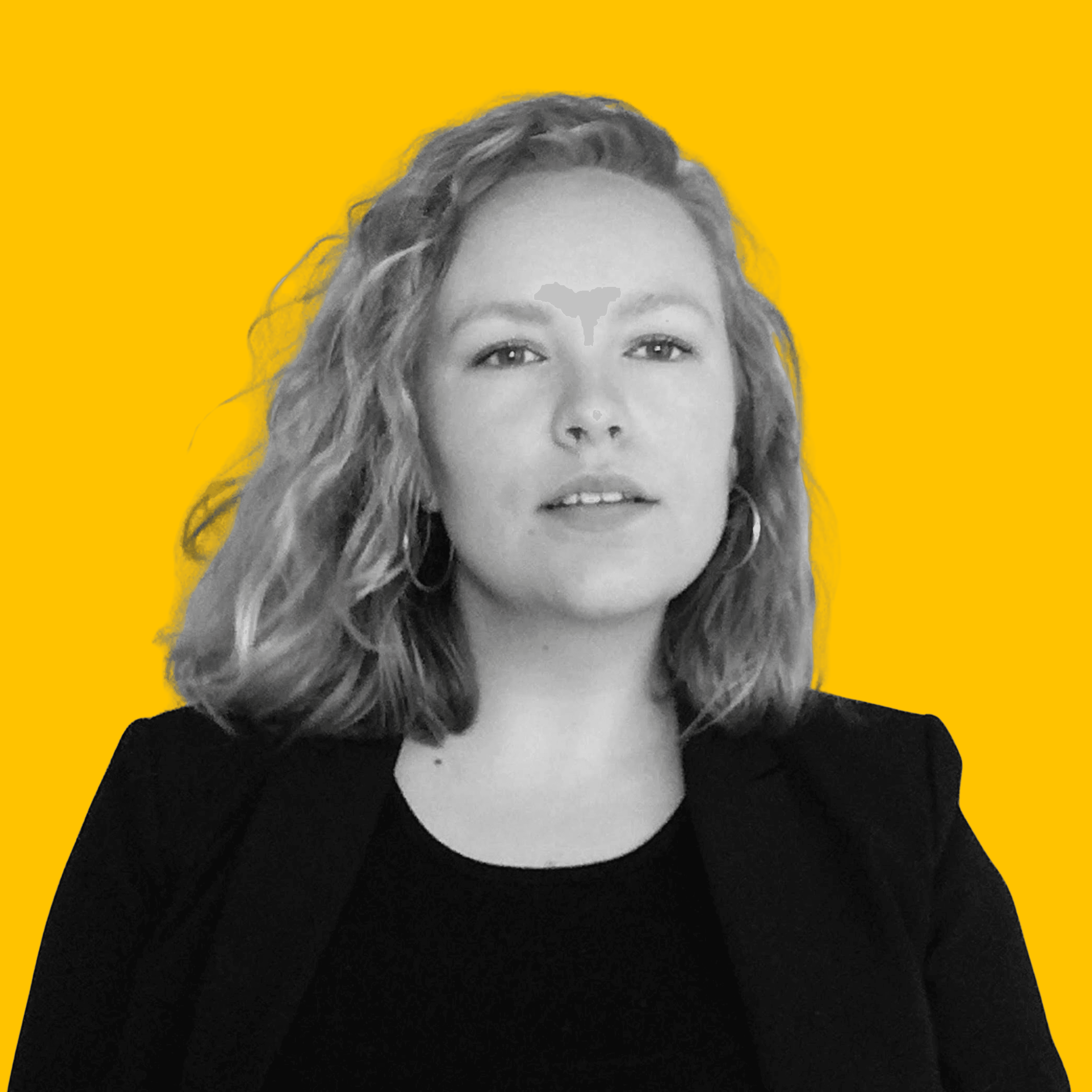 Black-and-white portrait of the designer on a yellow background, facing forward, wearing a dark blazer.