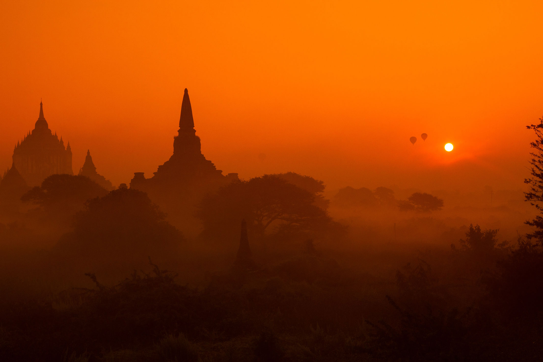 Silhouetted temples against an orange sunset sky, creating a serene and atmospheric landscape.