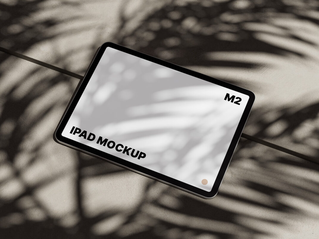 iPad mockup with a blank screen, displayed flat on a textured surface. The setting features dramatic palm leaf shadows cast by natural light, creating a tropical, minimalist aesthetic.