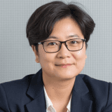 Headshot of a woman with short dark hair wearing glasses and a dark suit jacket.
