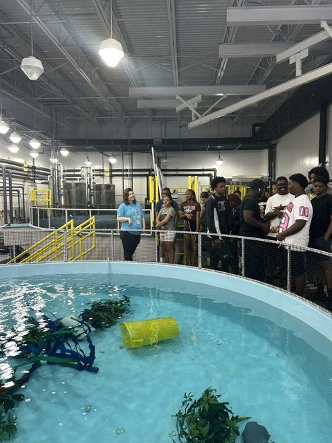 A group of young people touring an indoor aquaculture facility beside a large tank