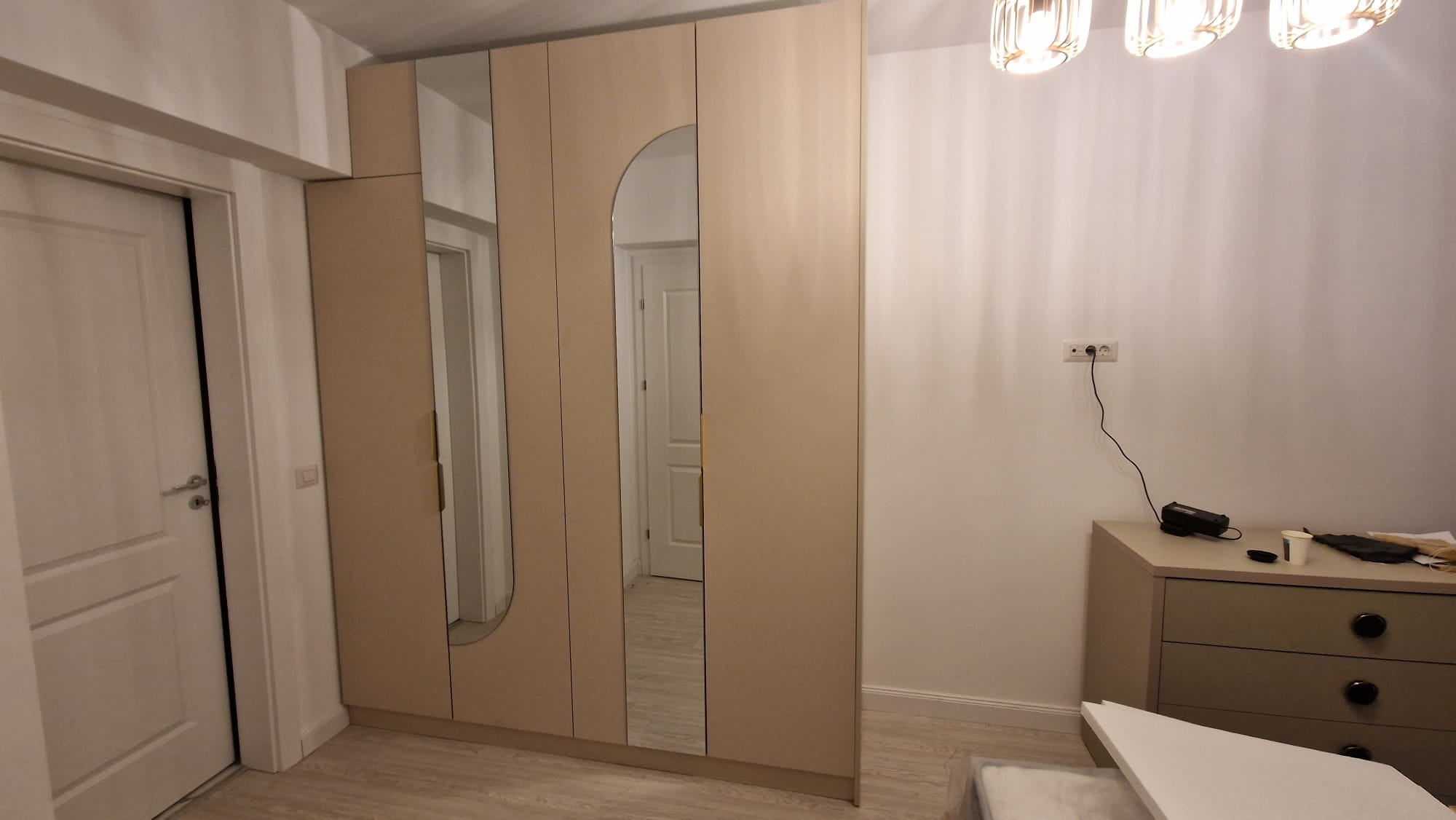 Dormitor cu dulapuri bej și oglinzi încorporate, comodă asortată și lumini calde.