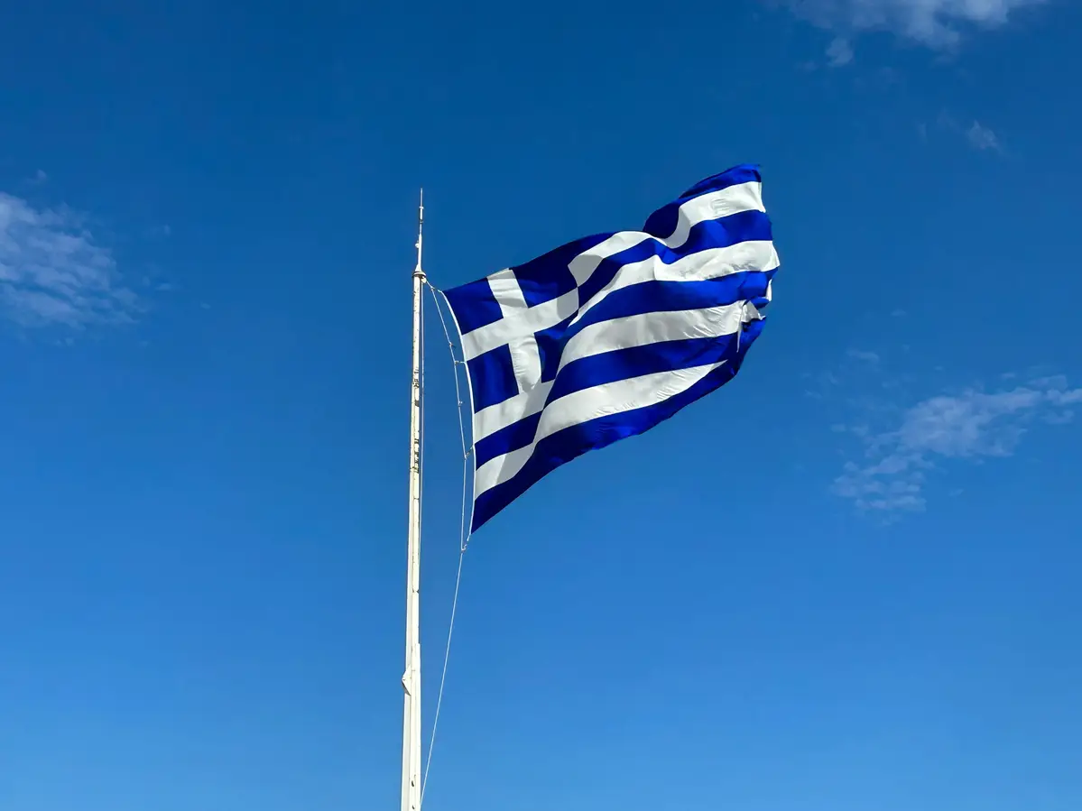 Drapeau grec flottant sur un mât contre un ciel bleu clair