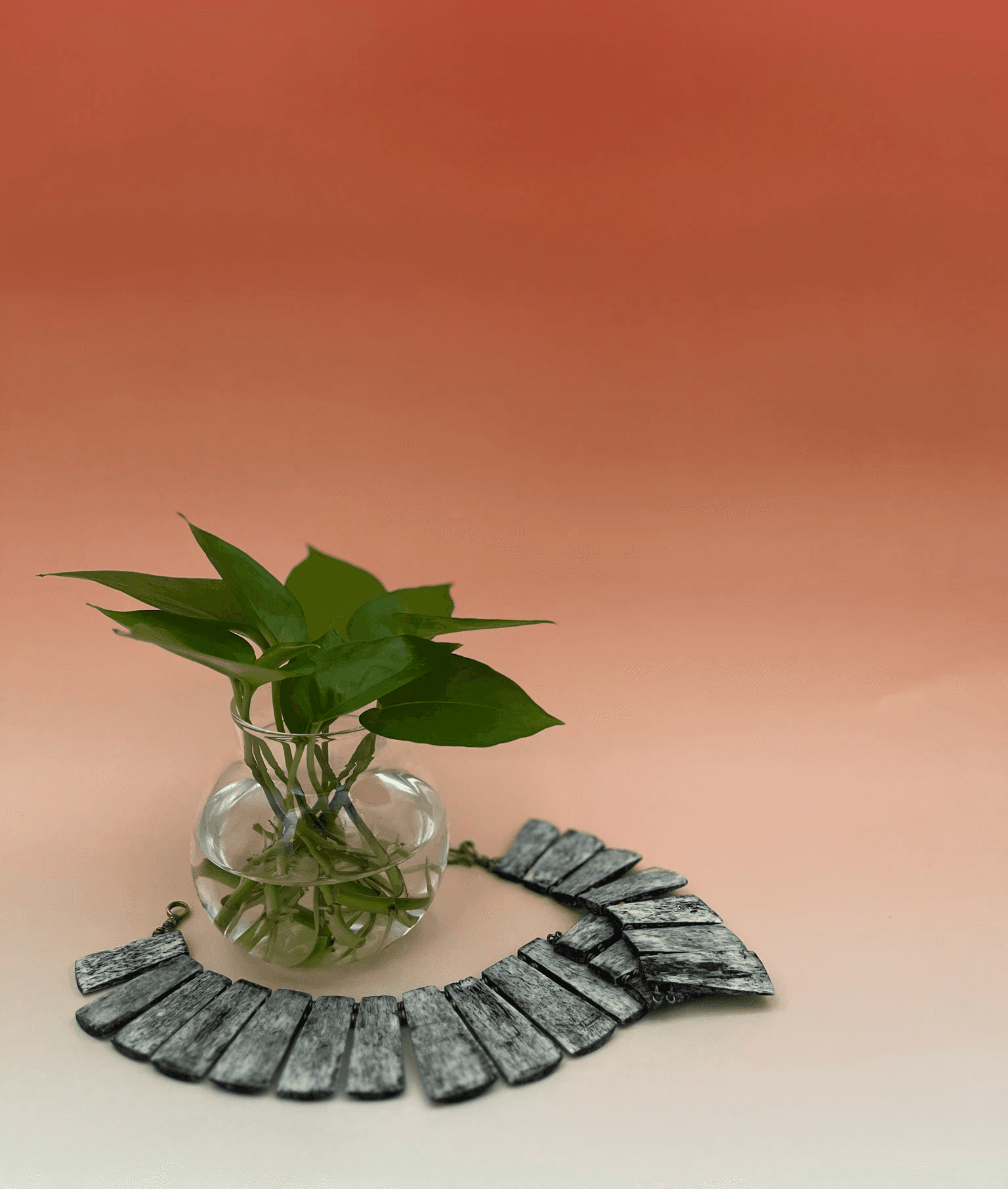 Necklace draped around glass jar filled with pothos leaves.
