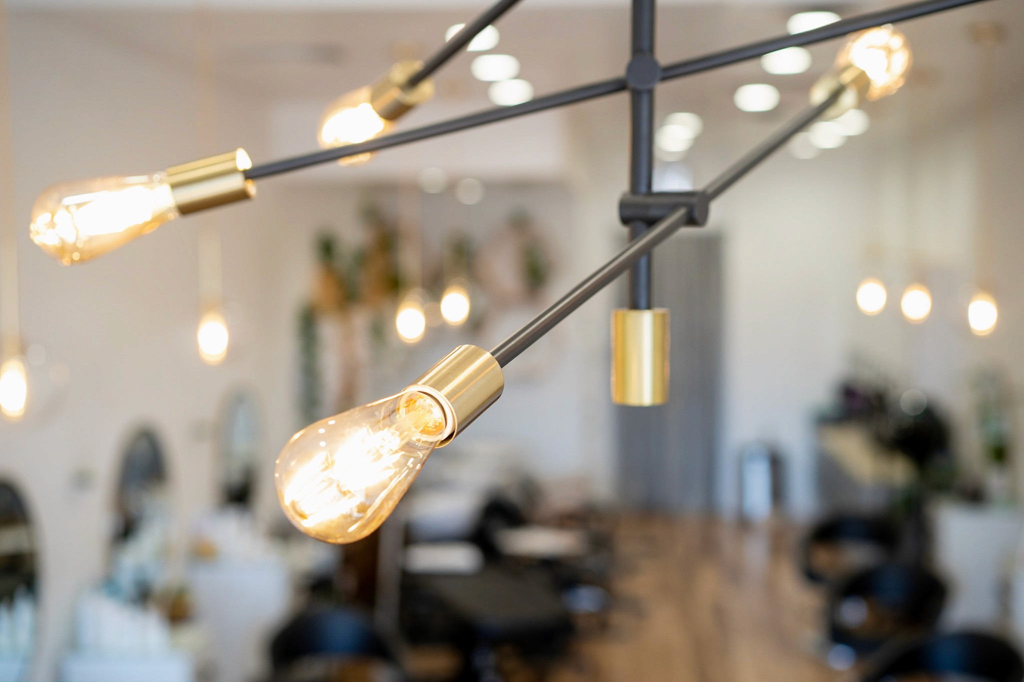 Close-up of a modern hanging light fixture at the entrance of Del Sol Hair Studio, with the salon interior softly blurred in the background for a warm, welcoming ambiance.