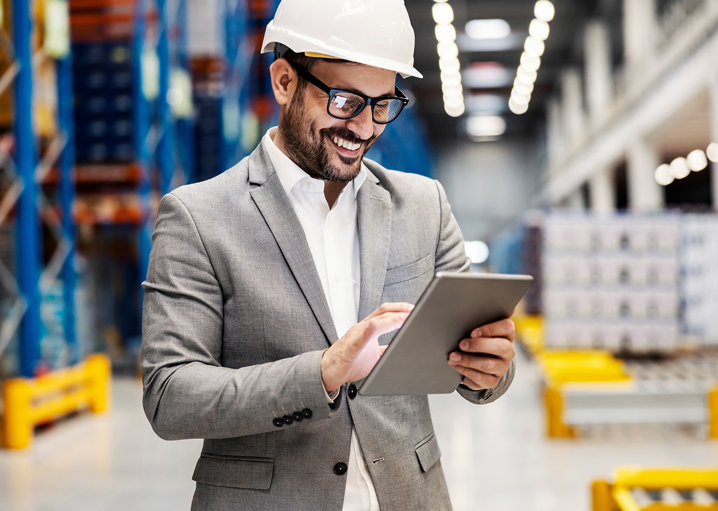 Titolare di un’azienda con aria soddisfatta sta gestendo da un pad le attività dell'azienda logistica, sullo sfondo vediamo il magazzino.