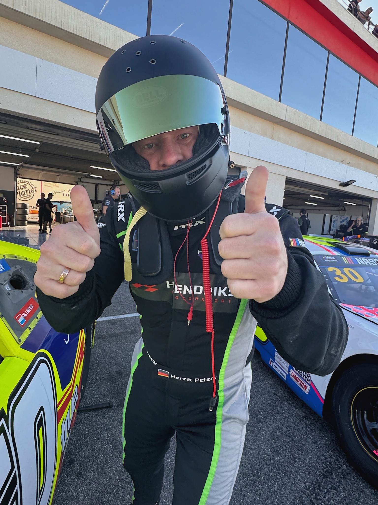 Henrik Peters in race suit and helmet beside the Hendriks Motorsport cars