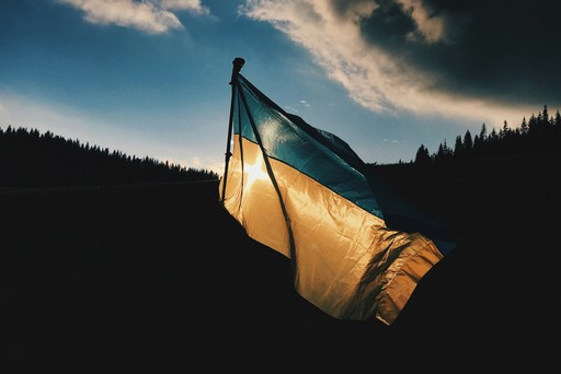 A flag gently waves against a dramatic sky, with silhouettes of hills in the background.