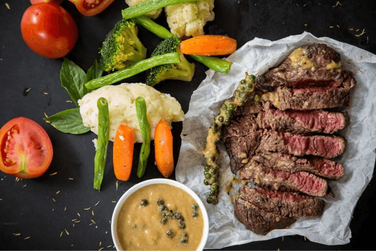 A plate full of steak, surrounded by vegetables and sauce.