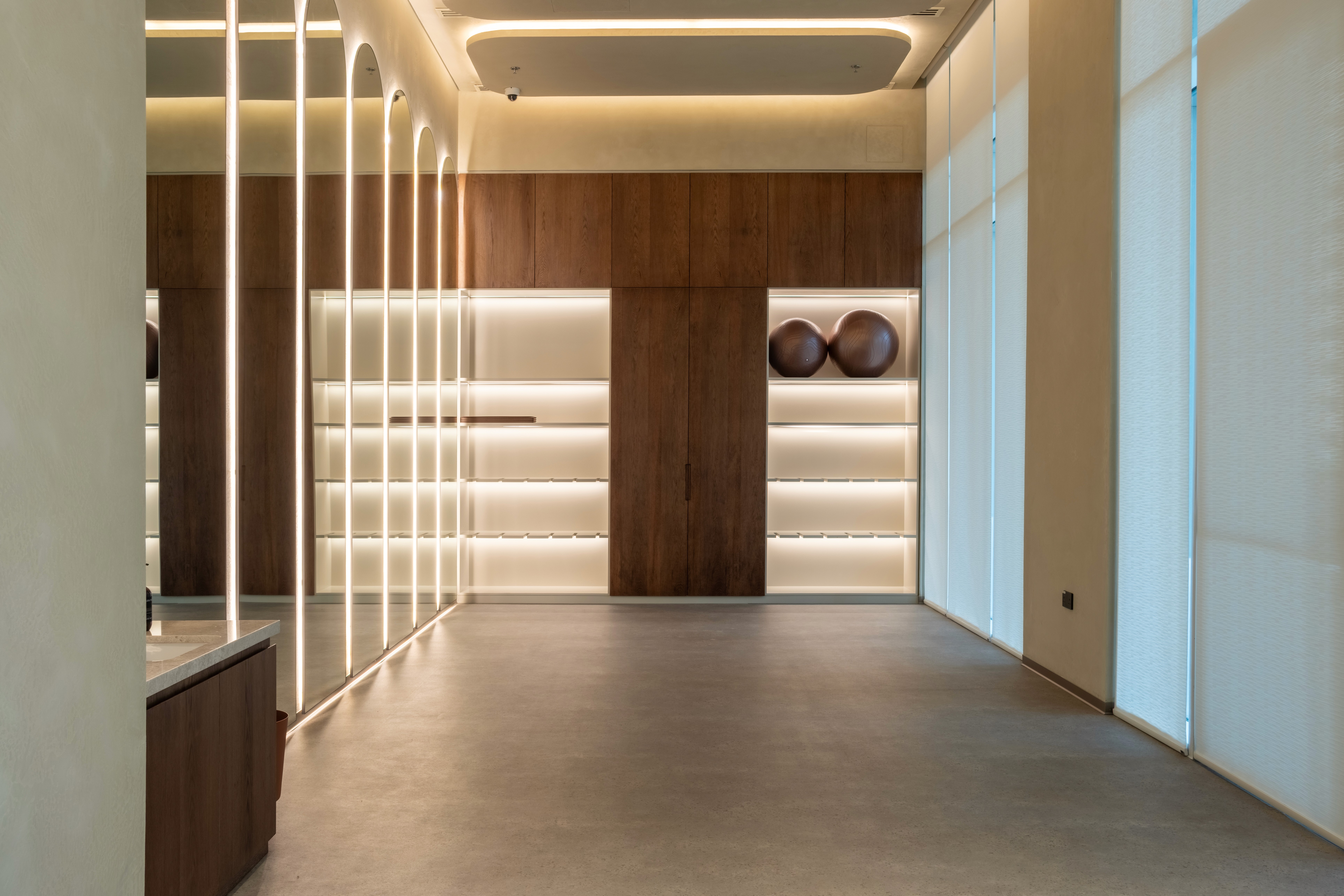 Intimate boutique gym with dark ribbed wood paneling, warm filament wall sconces, matte black equipment, dumbbell rack, and a light polished concrete floor