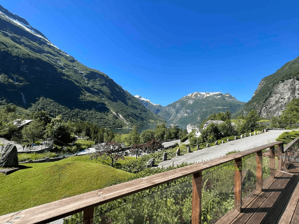 A panoramic view of lush green mountains under a clear blue sky, with wooden railings in the foreground.