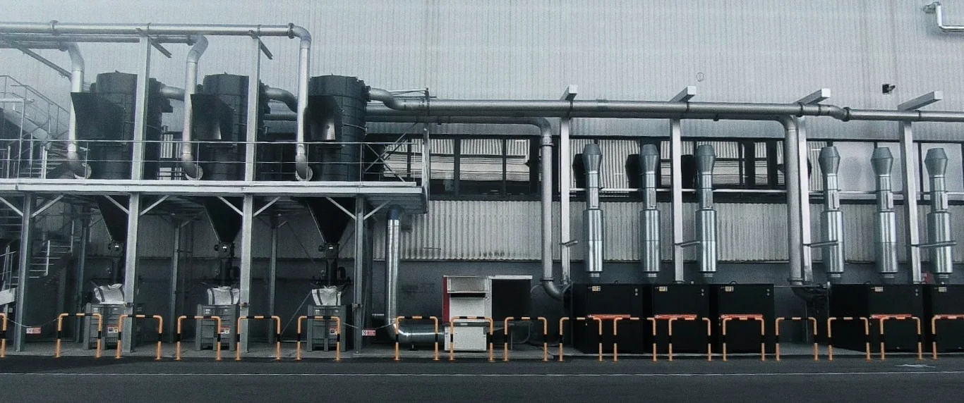Centrale d’aspiration industrielle extérieure avec plusieurs cyclones noirs, tuyauteries de collecte et équipements en pied de bâtiment.