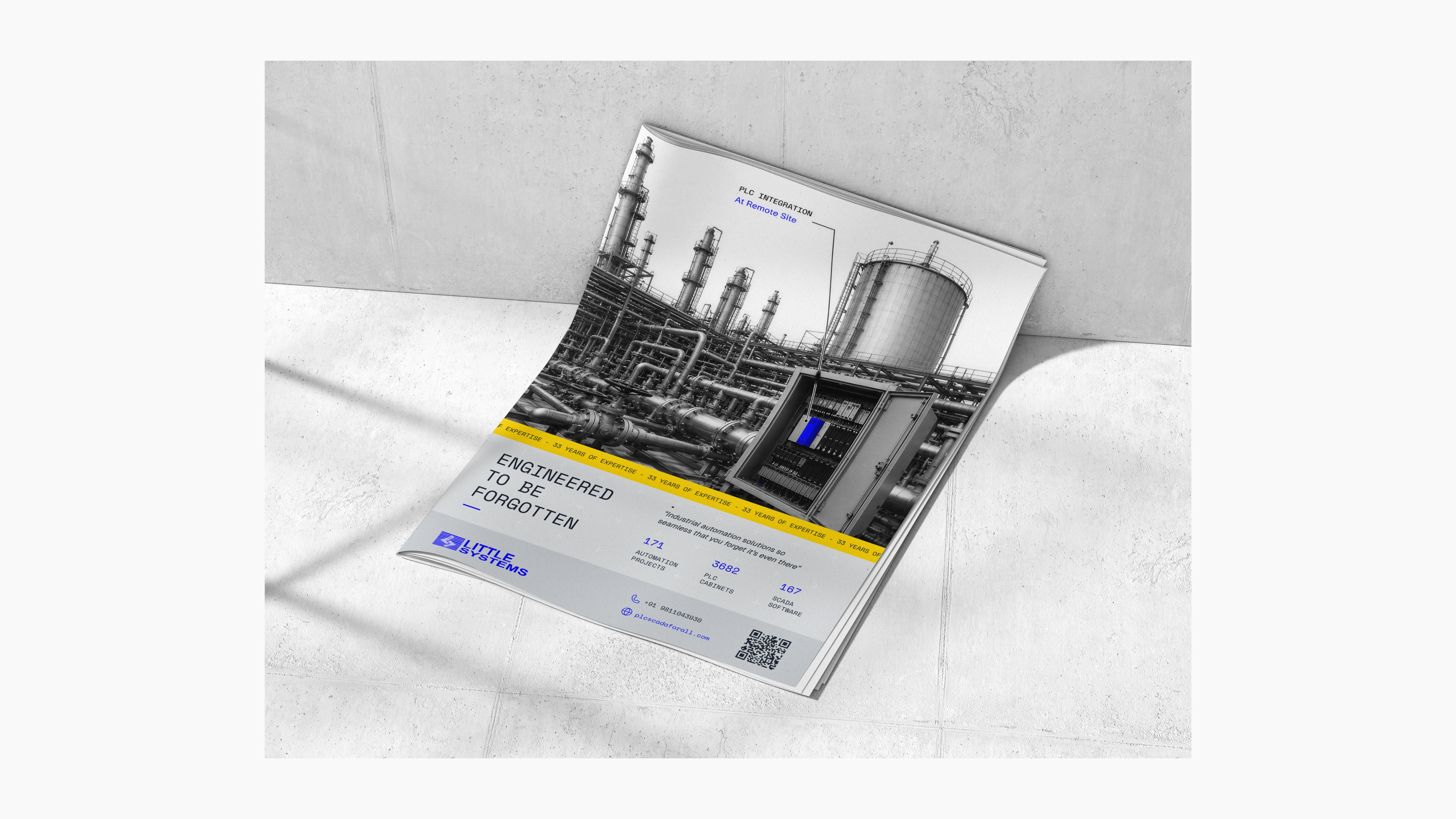 Open industrial brochure photographed on a concrete surface, featuring a black-and-white industrial plant photograph, technical annotations, blue and yellow accents, and Little Systems branding.