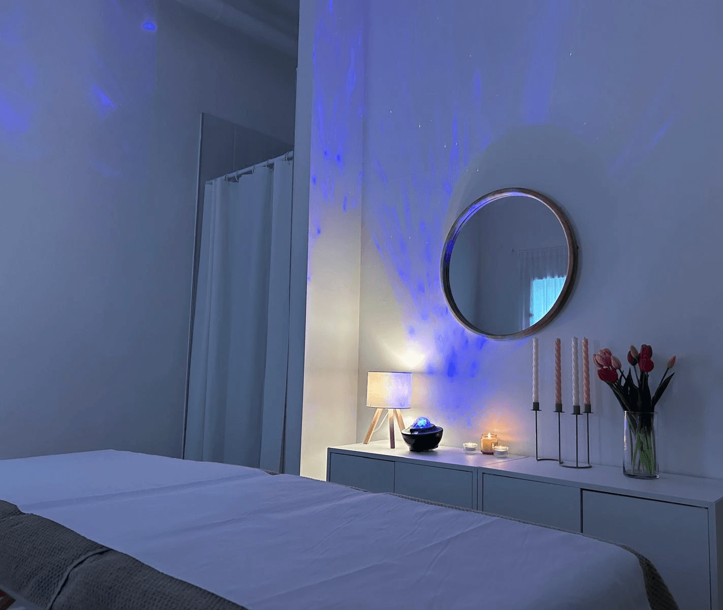 A serene and elegant spa space with wooden reclining chairs and white cushions. Golden sunlight filters through a cascading water feature, creating a peaceful atmosphere. Tropical plants and candles add to the relaxing ambiance.