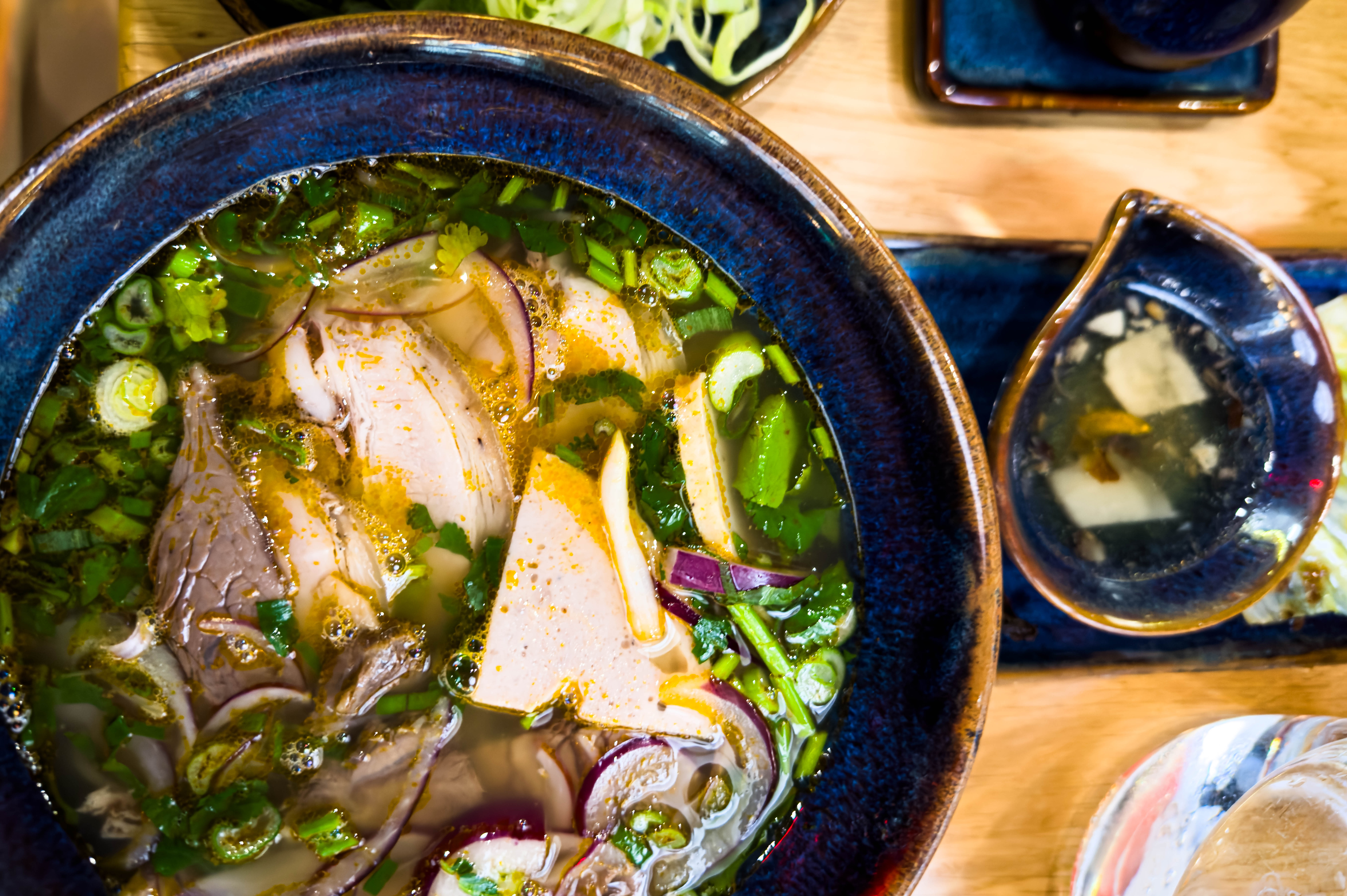 a bowl of beef pho in a big blue bowl on a blonde table