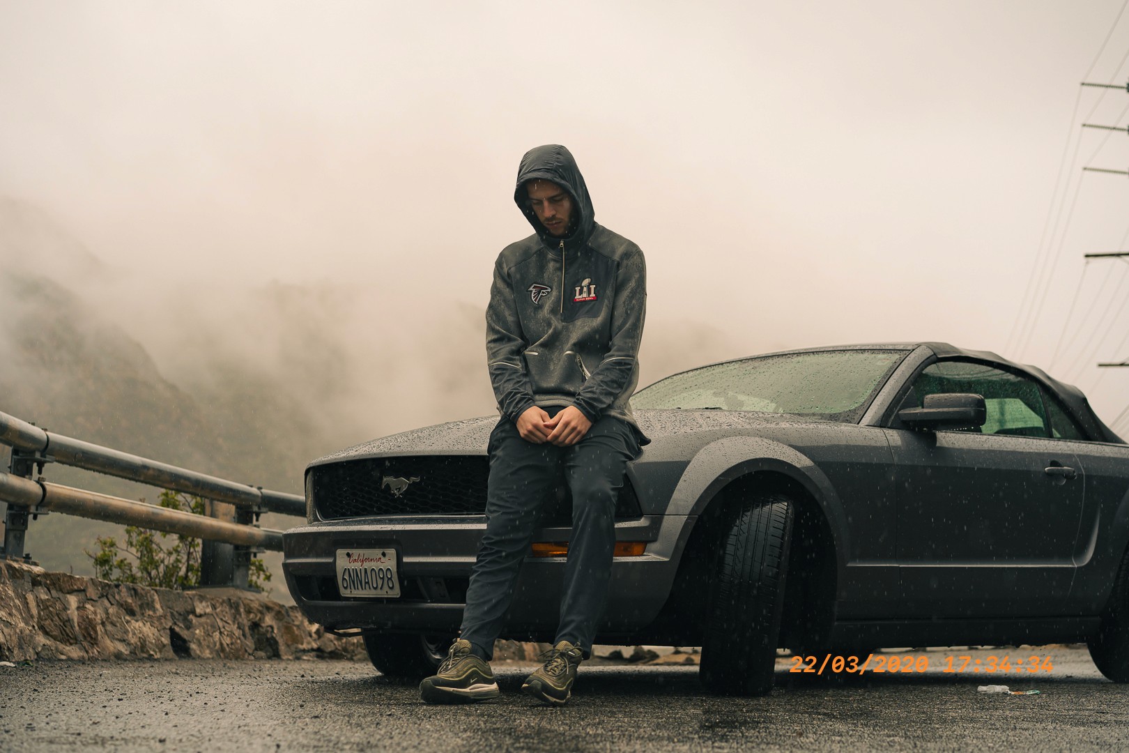 Portrait sous la pluie adossé à une Ford Mustang grise