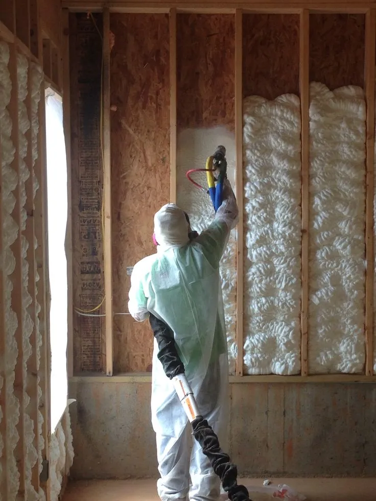 Technician applying spray foam insulation inside wall framing to improve energy efficiency