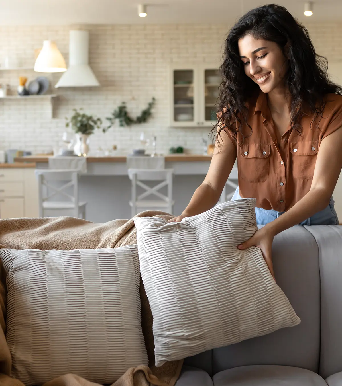 Woman styling a cozy living space with neutral throw pillows and soft textiles in a bright, modern home.