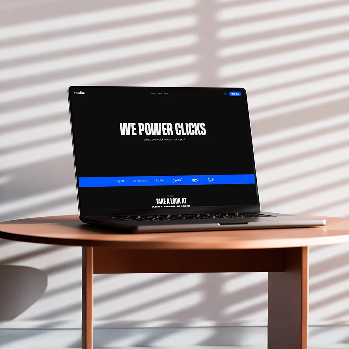 A laptop on a round table displaying a dark-themed marketing website with the headline “We Power Clicks.”