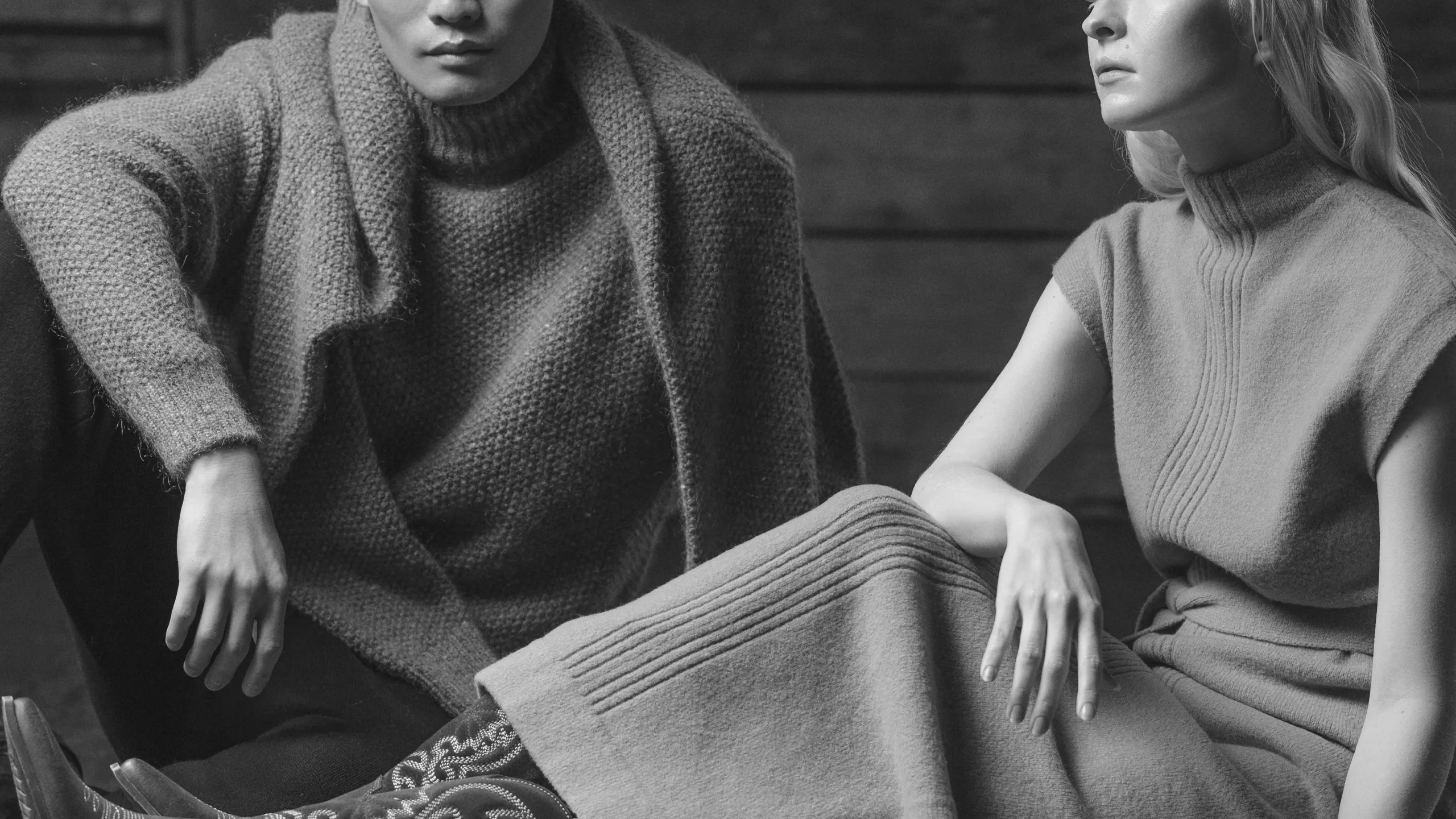 Two models wearing textured cashmere knitwear in neutral tones, seated in studio – Annapurna