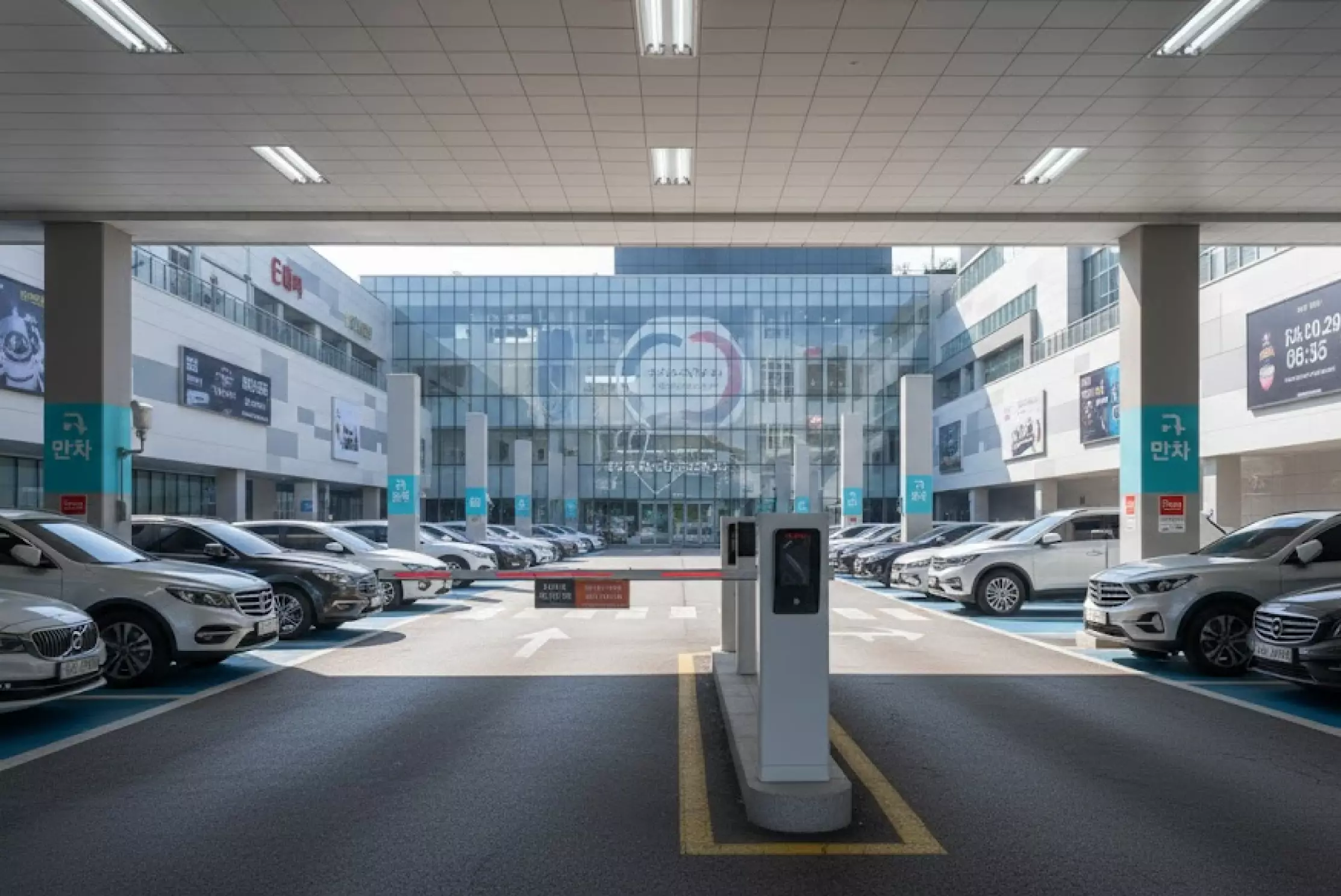 건물 입구 차단기와 차량이 정렬된 대형 상업시설 주차장 전경