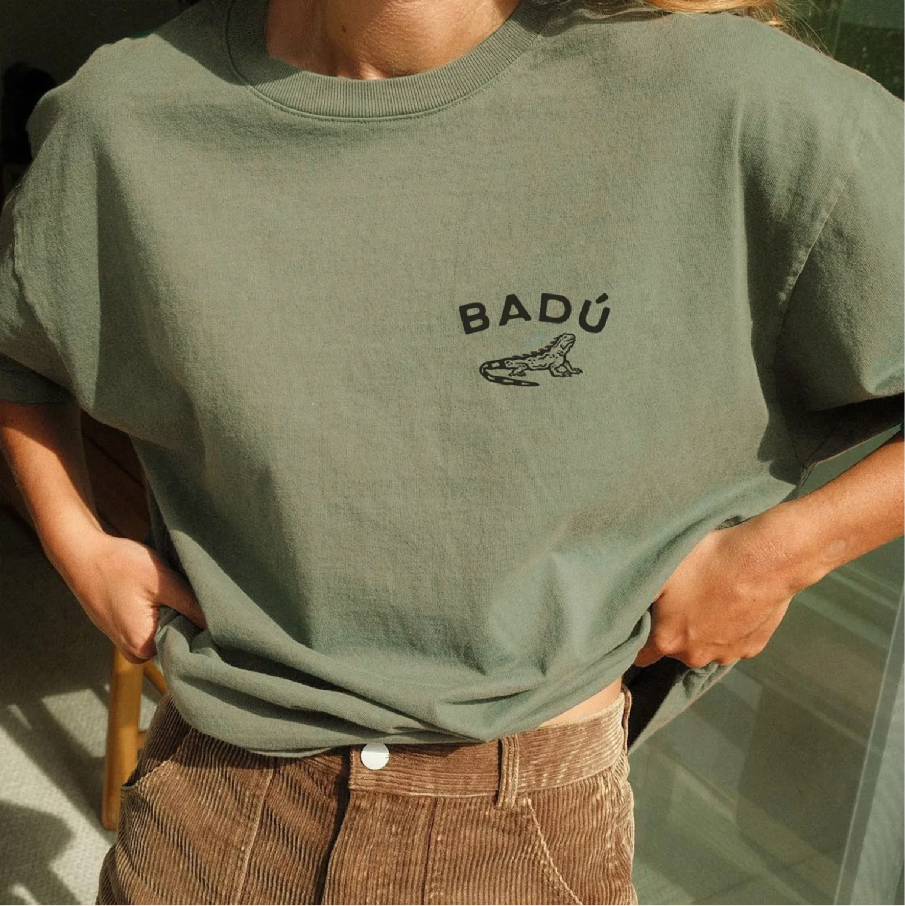 A green t-shirt with the badu logo and iguana icon printed on