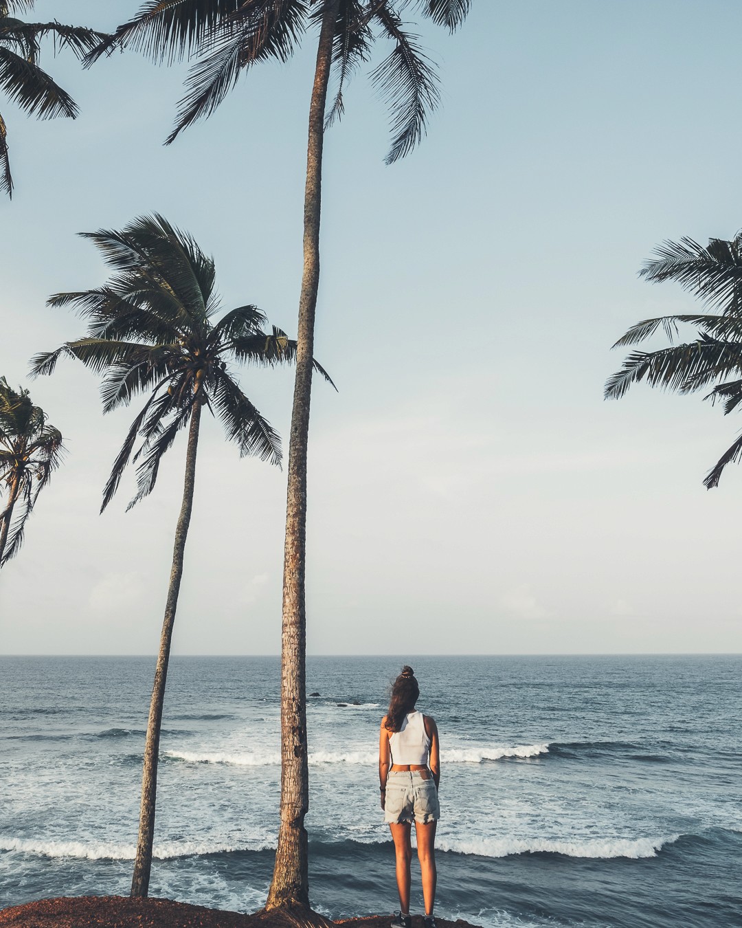 Eva gazing out at the ocean from a palm-lined tropical coast, inspiring mindful and adventurous travel.