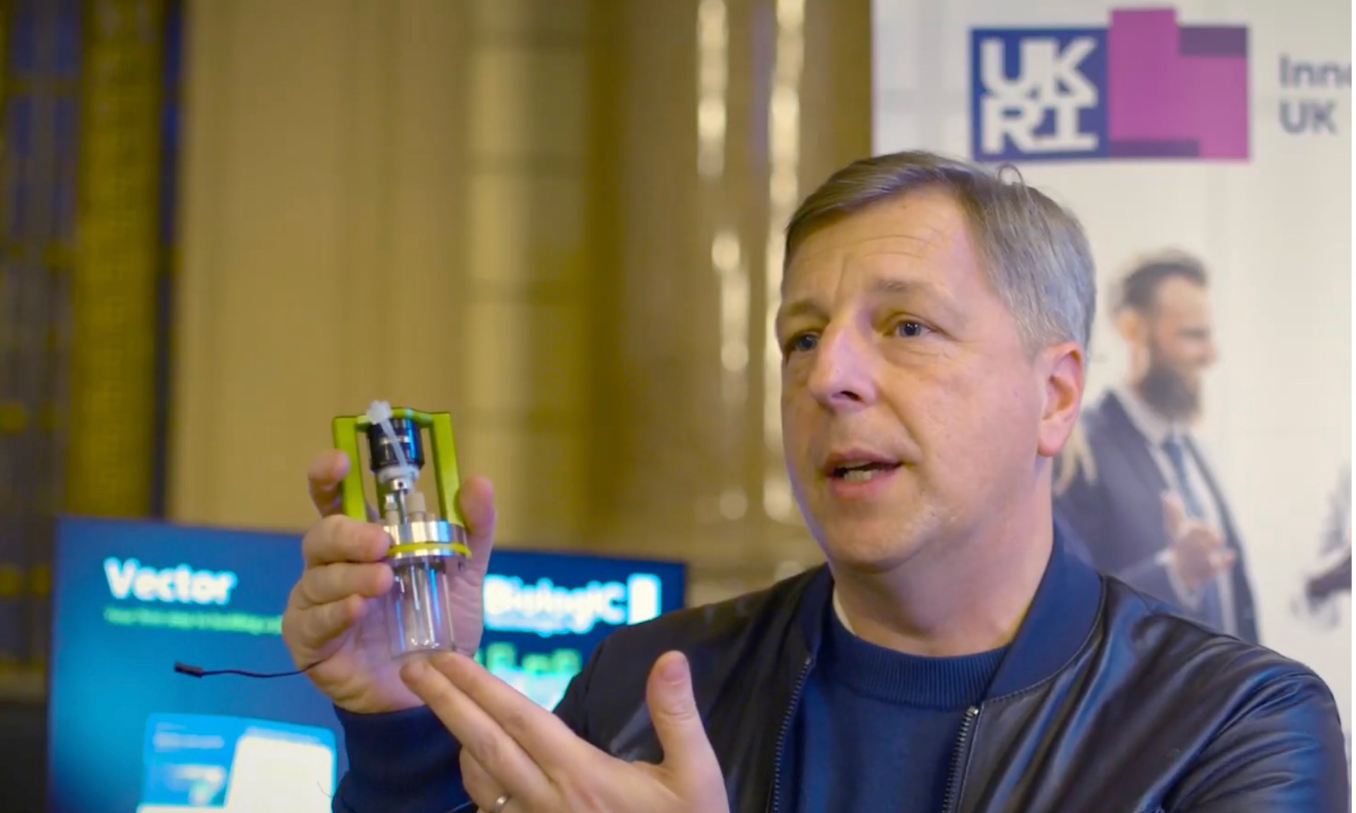 A photo of a man presenting a small scale bio-reactor at an exhibition