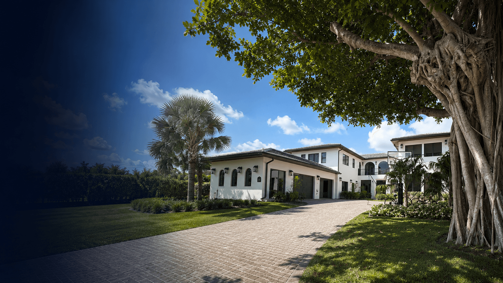 Large Mediterranean-style estate in Bay Point, with a paver driveway, arched windows, attached garage, mature shade tree, palm trees, and manicured lawn under a deep blue sky.