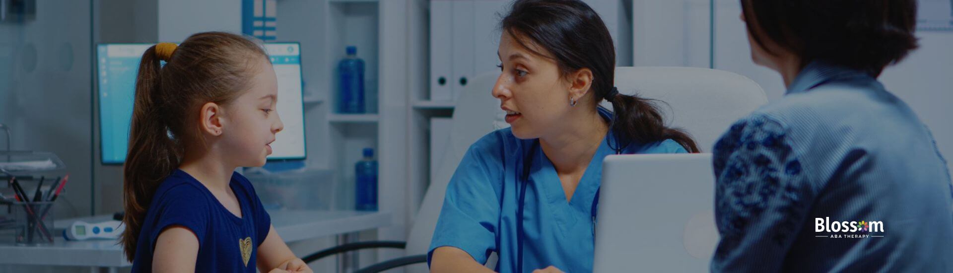 A young girl with autism sitting with a doctor and a parent during a consultation in a medical office.