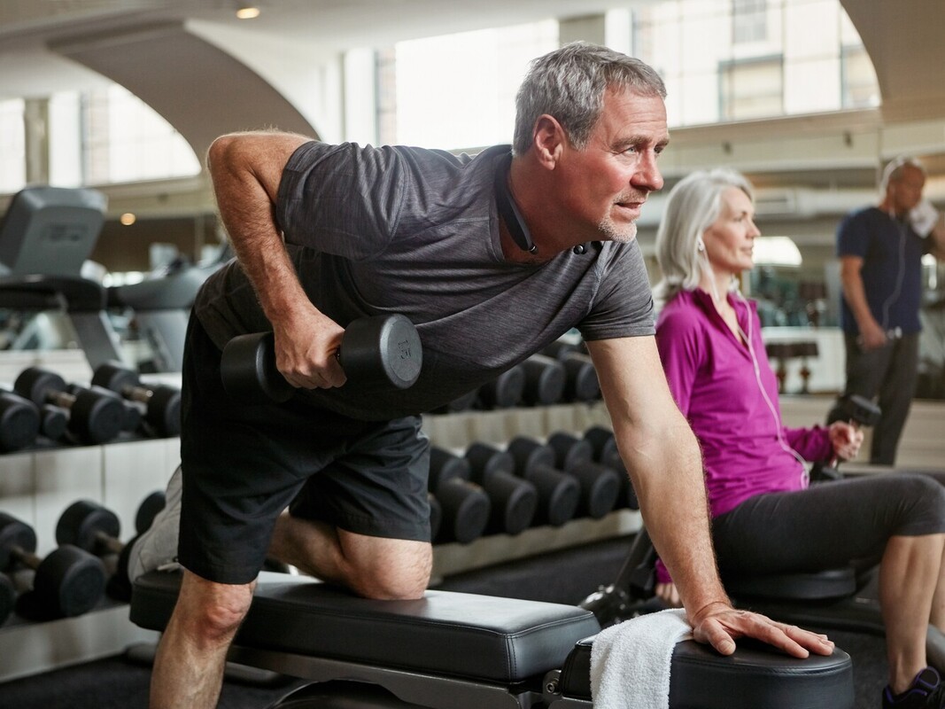 older man losing weight by running and doing complementary strength training with dumbbells in the gym