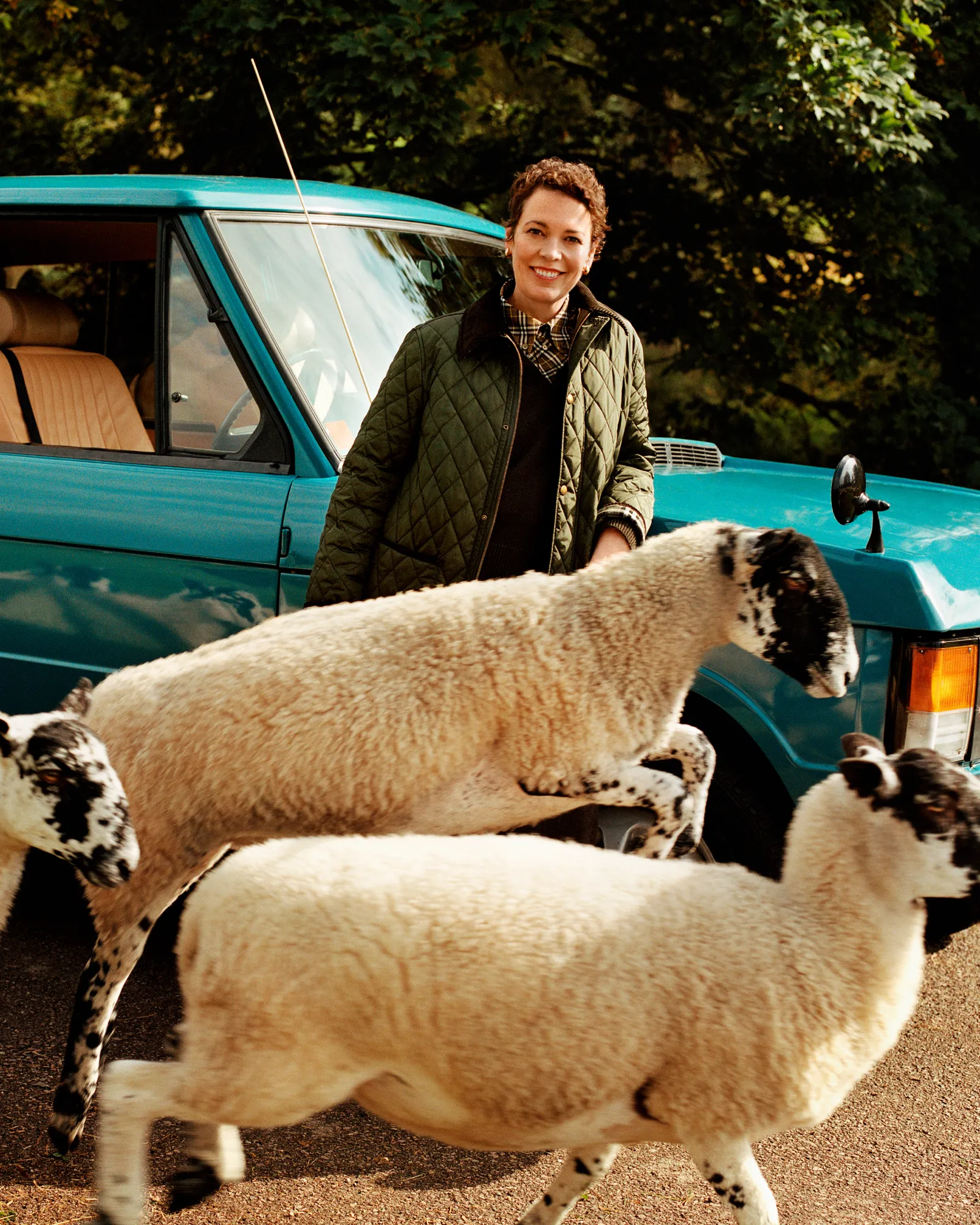 Woman standing beside a car as sheep cross the road