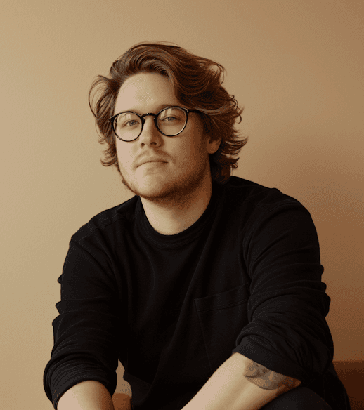A man with glasses sits comfortably on a couch, appearing thoughtful and at ease in his environment.
