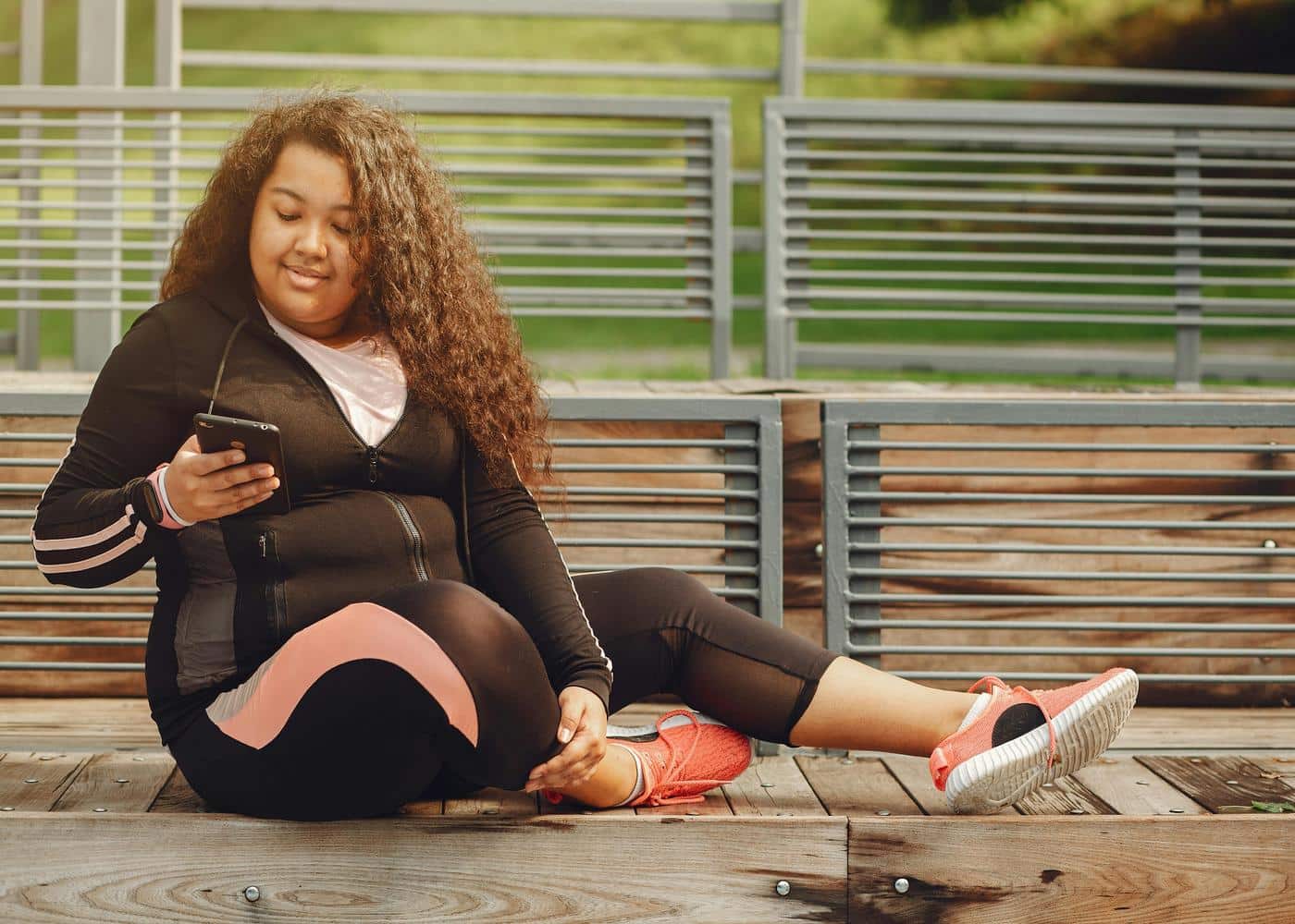 Woman in workout clothes sitting on ground outdoors while looking at smartphone