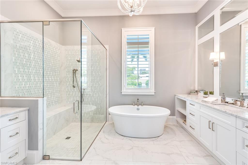 a high-end bathroom with a tub, shower room, and white cabinets with a window above the tub in the center