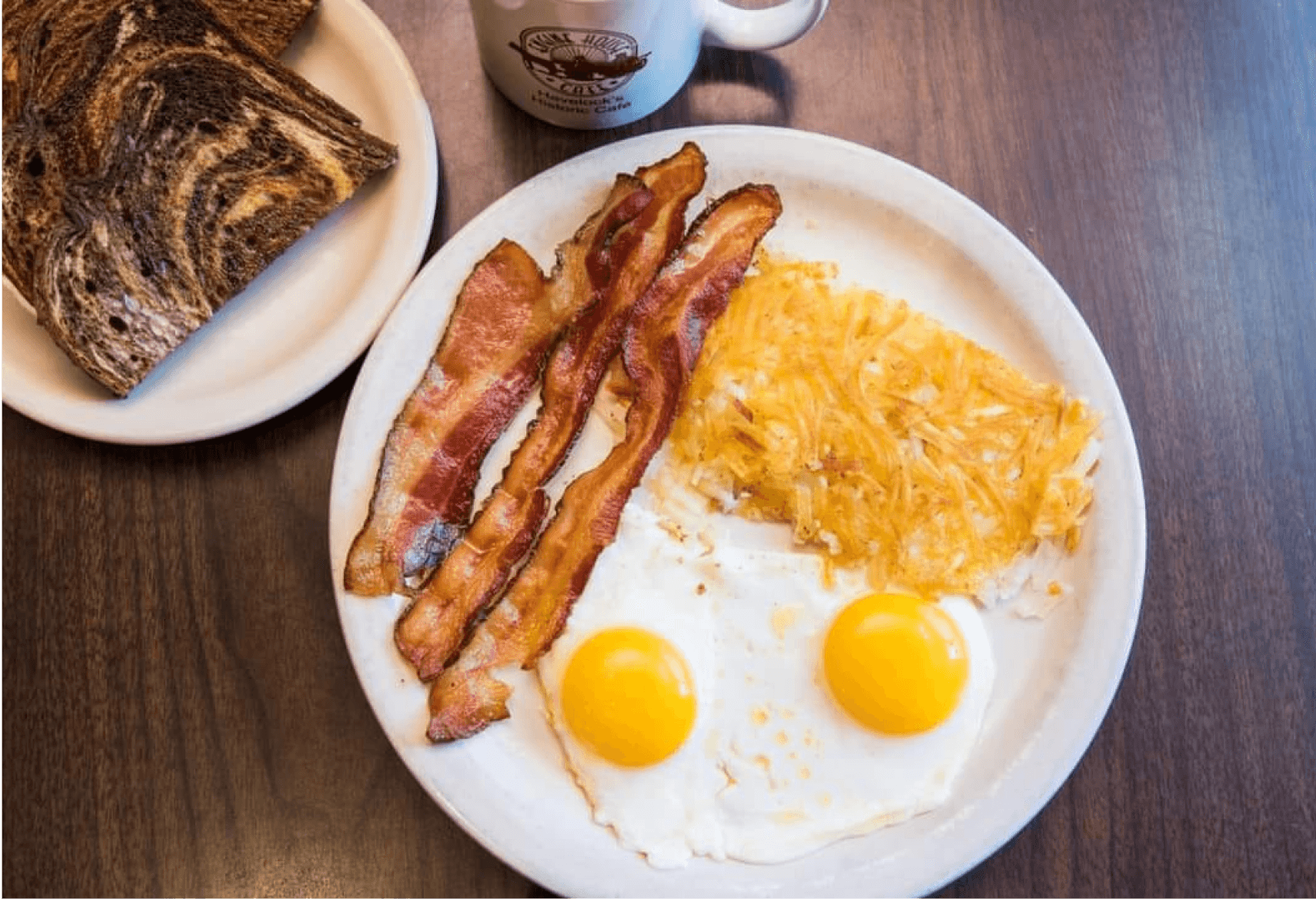 A hearty breakfast plate with two large eggs, crispy hash browns, bacon, and toast at Engine House Cafe