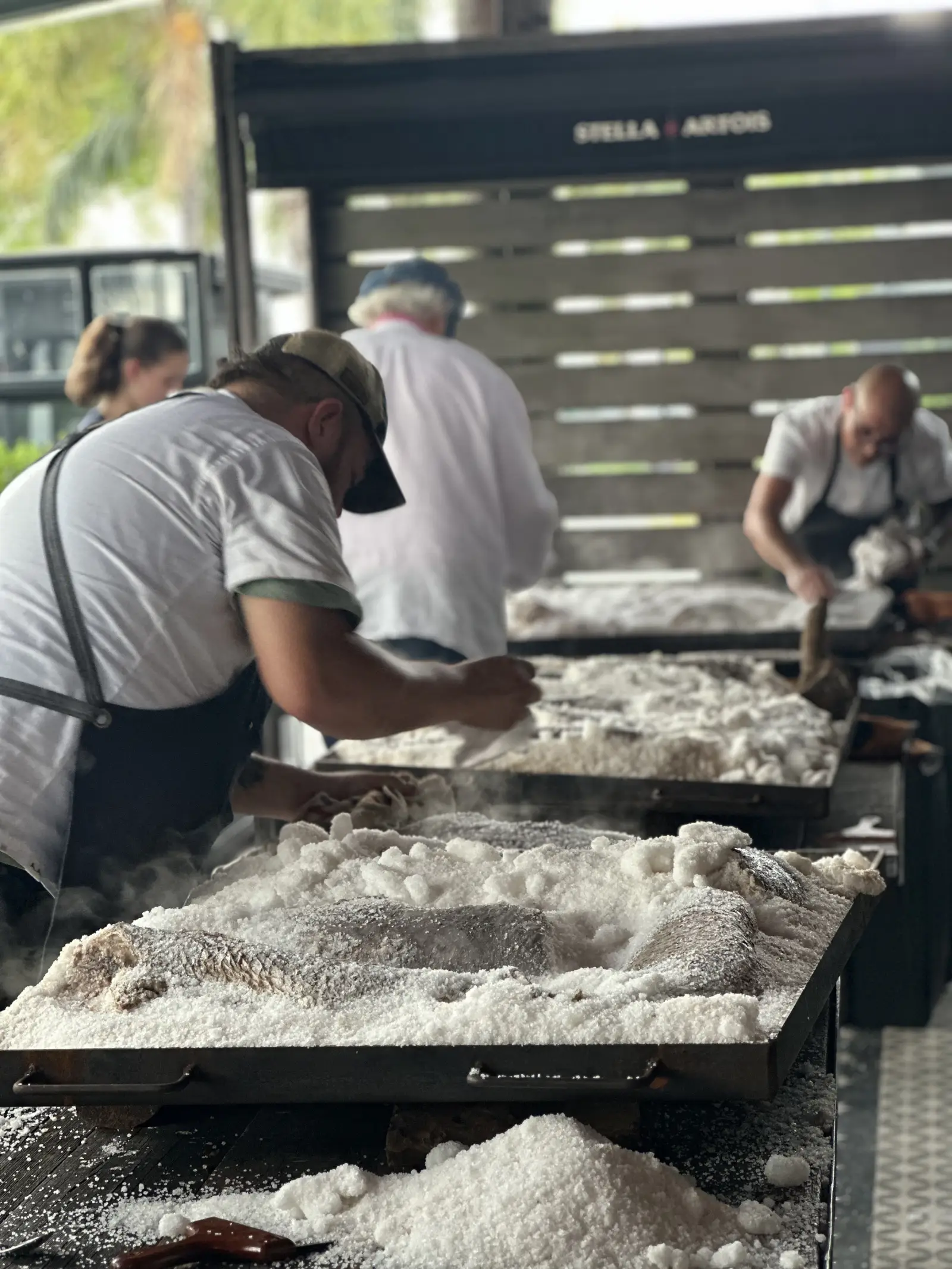 Primer plano de trabajadores cocinando pescado a la sal sobre brasas.