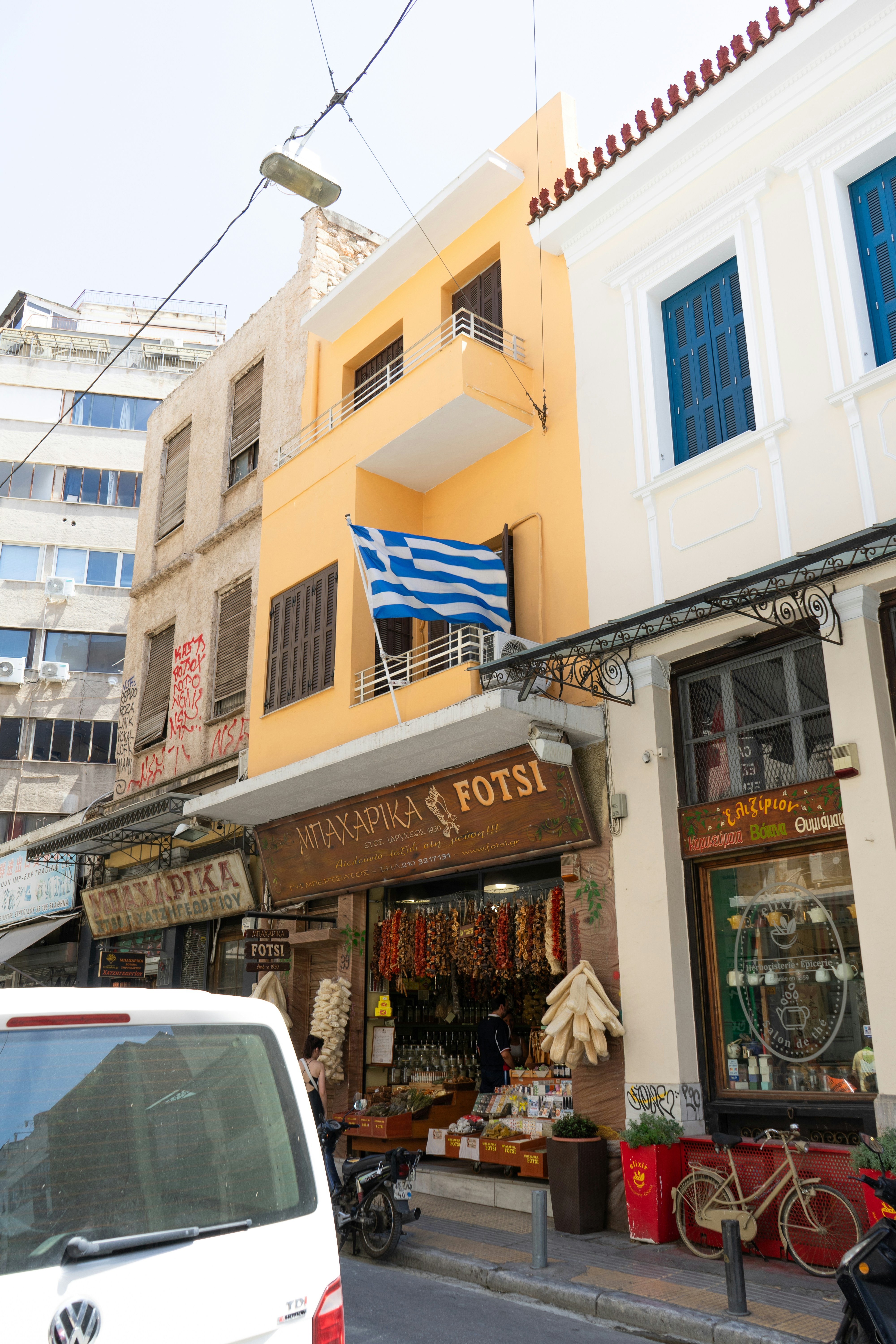 A greek flag flies over a storefront in athens.