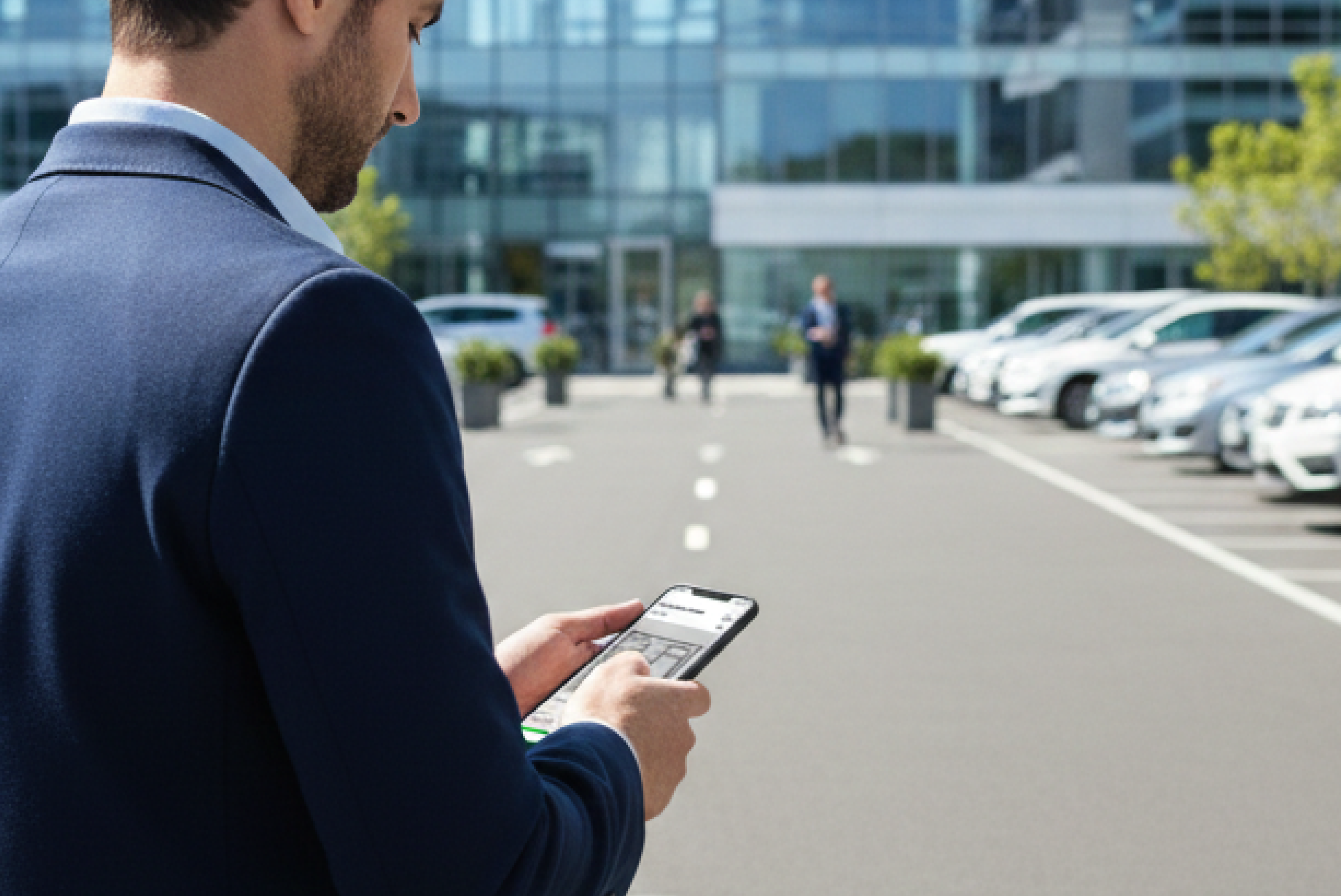 야외 주차장 앞에서 스마트폰으로 주차 관제 화면을 확인하는 관리자의 모습입니다.